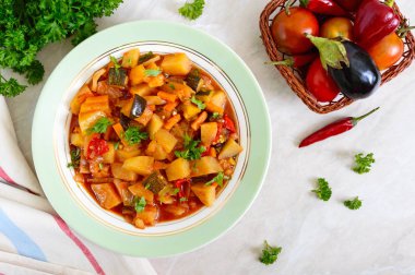 Masanın üzerine bir kase lezzetli sebze güveç. Demlenmiş patates, patlıcan, kabak, soğan, havuç, baharatlı domates soslu yeşillikleri ile.