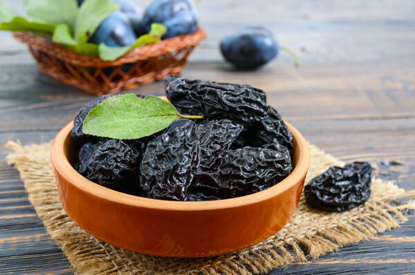 Prunes in a clay bowl and fresh plums, leaves on a wooden table. Fresh prunes for healthy life.
