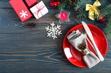 Noel tablo ayarı. Kırmızı tabak, çatal, bıçak, mum, peçete, koyu ahşap arka plan üzerinde bir Noel ağacı dalı hediyeler. Uzay kopyalayın. Noel Noel yılbaşı tatil arka plan.