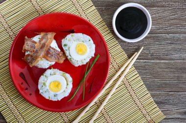 Dilim pastırma kırmızı plaka üzerinde yeşil soğan ile pirinç haşlanmış yumurta sarılı. Asya tarzı kahvaltı. Üstten görünüm