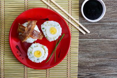 Dilim pastırma kırmızı plaka üzerinde yeşil soğan ile pirinç haşlanmış yumurta sarılı. Asya tarzı kahvaltı. Üstten görünüm