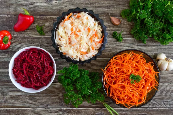 Salads from fresh vegetables: cabbage, carrots, beets. Korean spicy salads in bowls on a wooden table. Top view. Vitamin menu. Vegan cuisine.