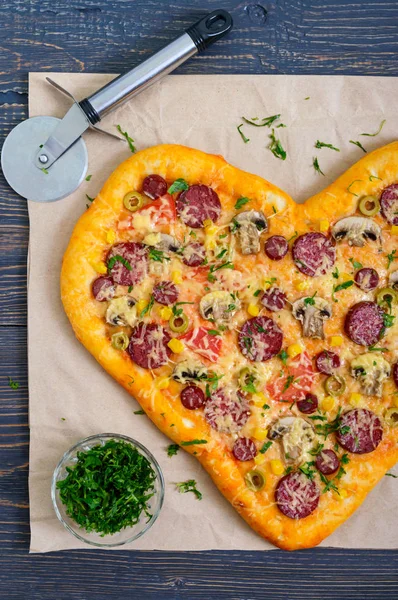 Tasty pizza in a heart shape with mushrooms, salami, pepperoni, olives, corn . The top view