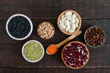 Sağlıklı gıda, diyet, beslenme kavramı, vegan protein kaynağı. Renkli ham Bakliyat Çeşitleri: kırmızı mercimek, yeşil bezelye, fasulye, nohut kase, ahşap bir masa üzerinde. Üstten görünüm, düz yatıyordu arka plan