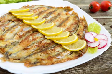 Pişmiş capelin ahşap bir masa üzerinde beyaz bir tabakta. Küçük balık bir fincan