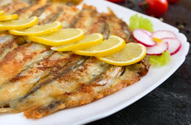 Kızarmış capelin siyah bir ahşap zemin üzerine beyaz bir tabakta limonlu. Küçük deniz balık bir tabak. Yakın çekim