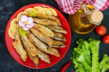 Kızarmış capelin siyah bir ahşap zemin üzerine kırmızı bir tabakta limonlu. Küçük deniz balık bir tabak. Üstten görünüm. Düz yatıyordu