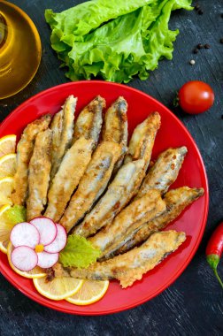 Kızarmış capelin siyah bir ahşap zemin üzerine kırmızı bir tabakta limonlu. Küçük deniz balık bir tabak. Üstten görünüm. Düz yatıyordu