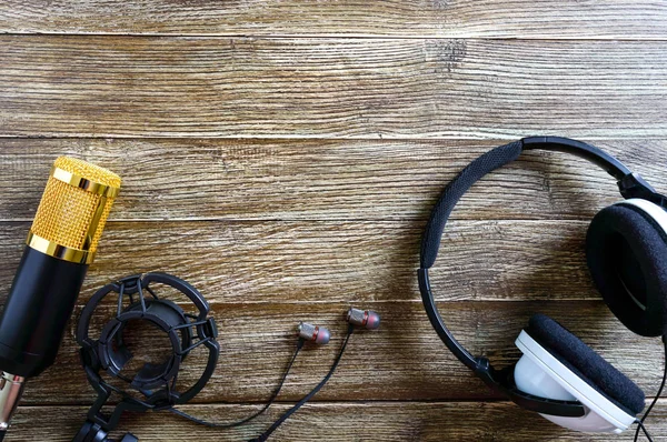 Condenser gold microphone  and headphones lies on a wooden table with copy space. Musical theme. Flat lay. Top view.