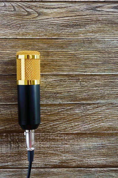 Condenser gold microphone lies on a wooden table with copy space. Musical theme. Flat lay. Top view.