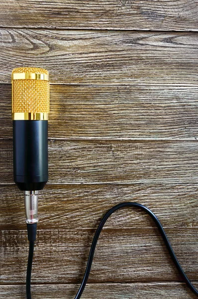 Condenser gold microphone with cable lies on a wooden table with copy space. Musical theme. Flat lay. Top view.