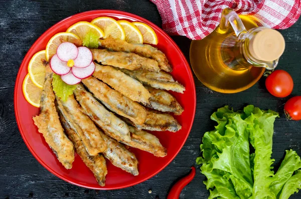 Kızarmış capelin siyah bir ahşap zemin üzerine kırmızı bir tabakta limonlu. Küçük deniz balık bir tabak. Üstten görünüm. Düz yatıyordu