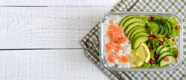 Lunch box: rice, salmon, salad with cucumber, avocado, greens on a white wooden background. Fitness food. The concept of healthy eating. School lunch box