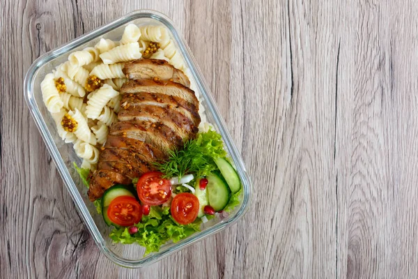 Lunch box: rotini with baked chicken breast and salad on a wooden background. Top view, flat lay. Delicious healthy lunch. The concept of healthy eating.