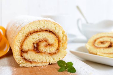 Beyaz ahşap bir masa üzerinde lezzetli bisküvi rulo ile kayısı reçeli. Kesme yakın çekim. Kahvaltıda tatlı.