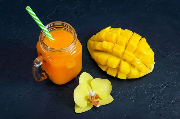 Mango smoothie in a glass jar and fresh mango on a black background. Mango shake. Tropical fruit concept.