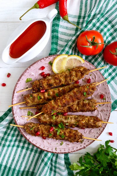 Tasty lula kebab on the plate on a white wooden table. Chopped meat on wooden skewers, grilled. Eastern cuisine. Top view, flat lay.