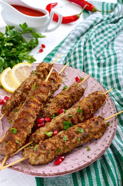 Tasty lula kebab on the plate on a white wooden table. Chopped meat on wooden skewers, grilled. Eastern cuisine.