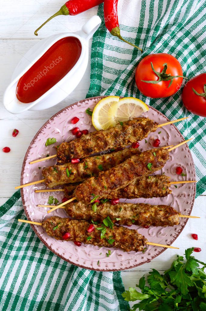 Tasty lula kebab on the plate on a white wooden table. Chopped meat on wooden skewers, grilled. Eastern cuisine. Top view, flat lay.