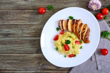 Izgara tavuk göğsü ve ahşap bir masa üzerinde beyaz bir tabak üzerinde lezzetli darı lapası. Üstte görüntü