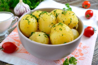 Ahşap bir masada bir kase tereyağı ve dereotu ile lezzetli haşlanmış genç patates.