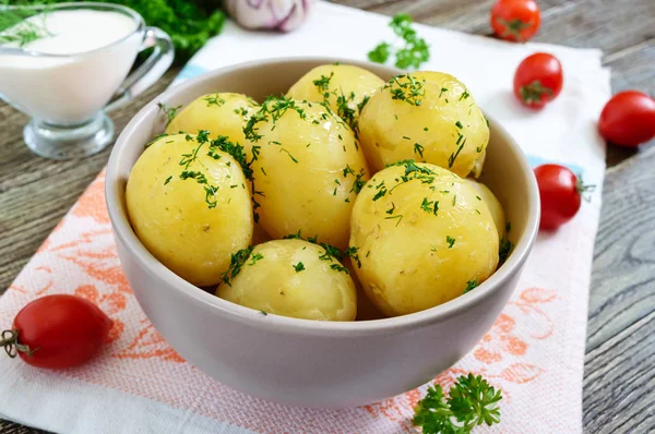 Ahşap bir masada bir kase tereyağı ve dereotu ile lezzetli haşlanmış genç patates.