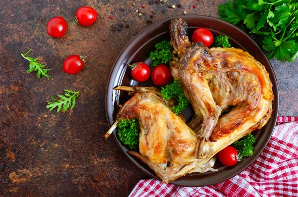 Bir tabaktabakta yeşillik ve domates ile bütün pişmiş tavşan. Lezzetli diyet eti. Üst görünüm, düz yatıyordu.