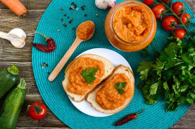 Bir kavanozda lezzetli kabak havyar ve masada beyaz ekmek dilimleri yayıldı. Kabak, sarımsak, havuç, domates soslu ev yapımı havyar. Vegan mutfağı. Üst teki görüş. Düz yatıyordu