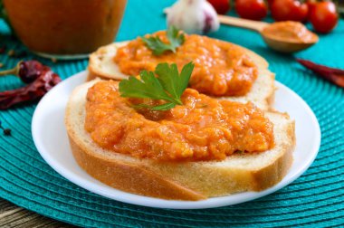 Bir kavanozda lezzetli kabak havyar ve masada beyaz ekmek dilimleri yayıldı. Kabak, sarımsak, havuç, domates soslu ev yapımı havyar. Vegan mutfağı. Yakın çekim