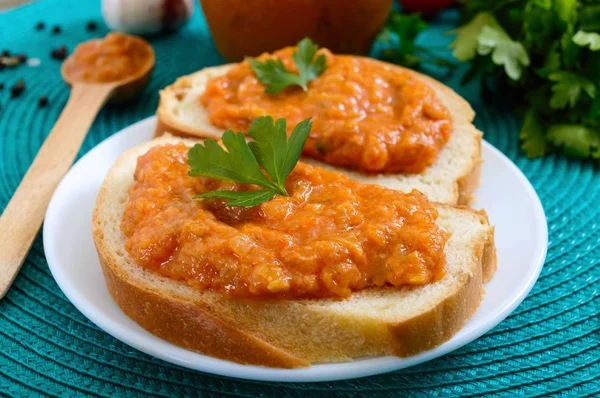 Delicious squash caviar in a jar and spread on slices of white bread on the table. Homemade caviar with zucchini, garlic, carrots, tomato sauce. Vegan cuisine. Close up