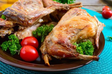 Bir tabaktabakta yeşillik ve domates ile bütün pişmiş tavşan. Lezzetli diyet et.