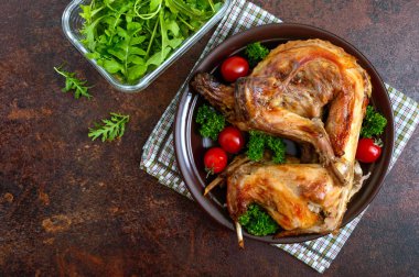 Bir tabaktabakta yeşillik ve domates ile bütün pişmiş tavşan. Lezzetli diyet eti. Üst görünüm, düz yatıyordu.