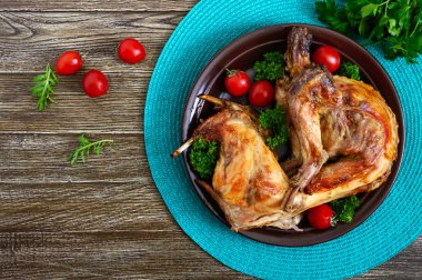 Bir tabaktabakta yeşillik ve domates ile bütün pişmiş tavşan. Lezzetli diyet eti. Üst görünüm, düz yatıyordu.