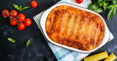 Beşamel soslu cannelloni dolması. Cannelloni makarna et, krema sosu, siyah bir arka plan üzerinde peynir ile pişmiş. Üst görünüm, düz yatıyordu.