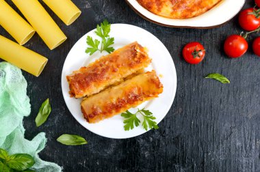 Beşamel soslu cannelloni dolması. Cannelloni makarna et, krema sosu, siyah bir arka plan üzerinde peynir ile pişmiş. Üst görünüm, düz yatıyordu.