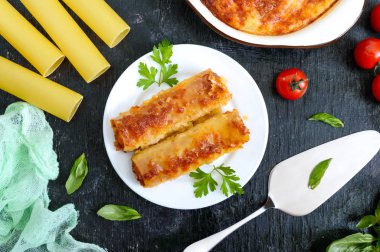 Beşamel soslu cannelloni dolması. Cannelloni makarna et, krema sosu, siyah bir arka plan üzerinde peynir ile pişmiş. Üst görünüm, düz yatıyordu.