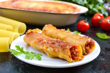 Beşamel soslu cannelloni dolması. Cannelloni makarna et, krema sosu, siyah bir arka plan üzerinde peynir ile pişmiş