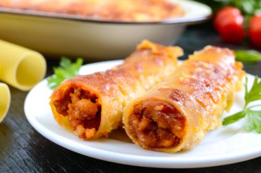 Beşamel soslu cannelloni dolması. Cannelloni makarna et, krema sosu, siyah bir arka plan üzerinde peynir ile pişmiş