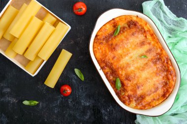 Beşamel soslu cannelloni dolması. Cannelloni makarna et, krema sosu, siyah bir arka plan üzerinde peynir ile pişmiş. Üst görünüm, düz yatıyordu.