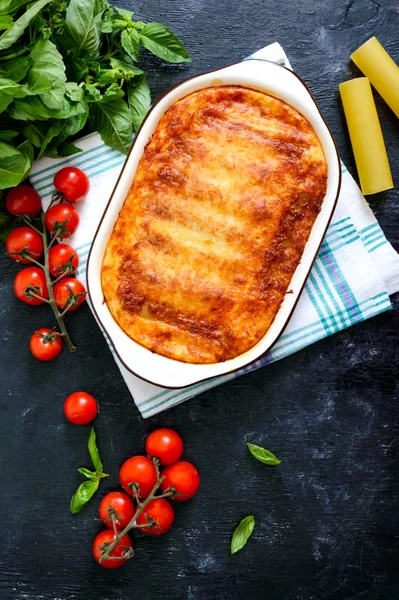 Beşamel soslu cannelloni dolması. Cannelloni makarna et, krema sosu, siyah bir arka plan üzerinde peynir ile pişmiş. Üst görünüm, düz yatıyordu.