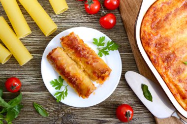 Beşamel sosu ile doldurulmuş içindeki cannelloni. Ahşap arka planda et, krem sos, peynir ile pişmiş cannelloni makarna. Üst görünüm, düz yatıyordu.