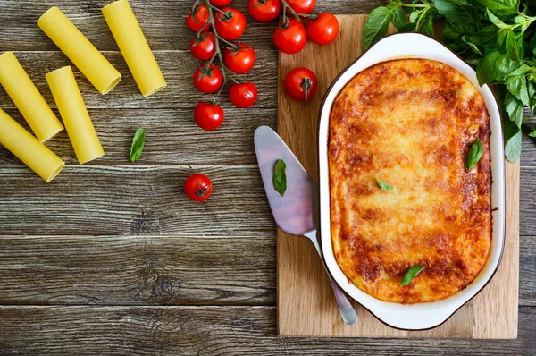 Beşamel sosu ile doldurulmuş içindeki cannelloni. Ahşap arka planda et, krem sos, peynir ile pişmiş cannelloni makarna. Üst görünüm, düz yatıyordu.