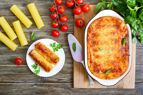 Beşamel sosu ile doldurulmuş içindeki cannelloni. Ahşap arka planda et, krem sos, peynir ile pişmiş cannelloni makarna. Üst görünüm, düz yatıyordu.