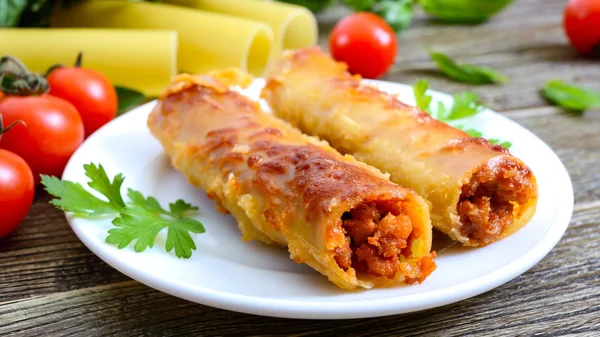 Beşamel sosu ile doldurulmuş içindeki cannelloni. Ahşap arka planda et, krem sos, peynir ile pişmiş cannelloni makarna.