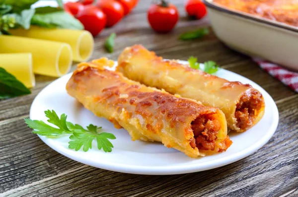 Beşamel sosu ile doldurulmuş içindeki cannelloni. Ahşap arka planda et, krem sos, peynir ile pişmiş cannelloni makarna.