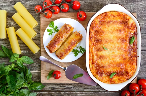 Beşamel sosu ile doldurulmuş içindeki cannelloni. Ahşap arka planda et, krem sos, peynir ile pişmiş cannelloni makarna. Üst görünüm, düz yatıyordu.
