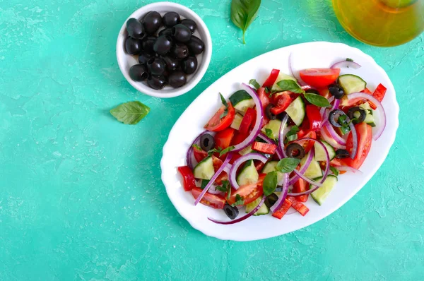 Tasty vitamin vegan salad of tomato, cucumber, red onion, black olives, basil sauce on a white plate on a bright background. Top view, flat lay