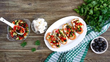 Ahşap bir arka plan üzerinde beyaz bir tabak üzerinde domates ve feta ile Klasik bruschetta. Tost baget, keçi peyniri, taze sebze, fesleğen ile İtalyan sandviç. Üst görünüm, düz yatıyordu. Afiş