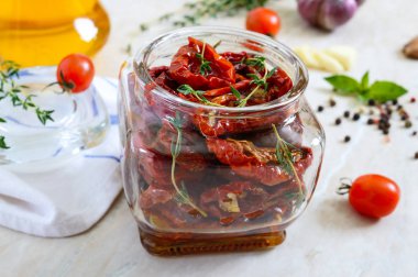 Otlar ile güneşte kurutulmuş domates, hafif bir arka plan üzerinde cam bir kavanozda zeytinyağı sarımsak.