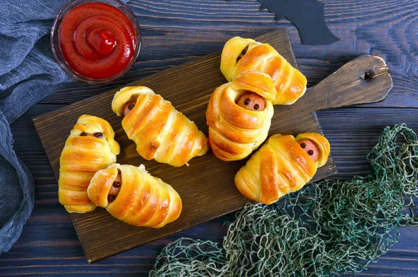 Funny sausage mummies in dough with ketchup on table. Halloween food. Top view. Flat lay